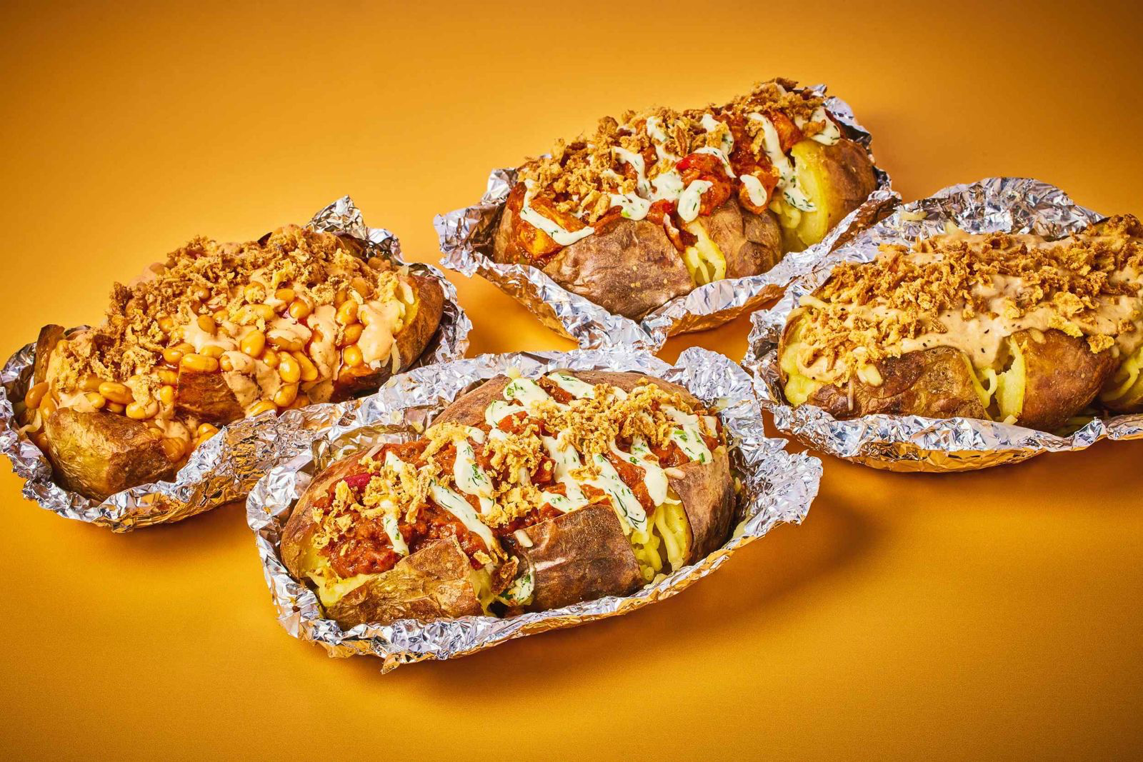 Foil-wrapped jacket potatoes loaded with toppings like beans, sauces, and crispy onions